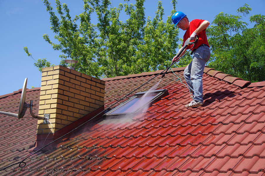 House Roof Cleaning With Pressure Tool. Worker On Top Of Buildin House roof cleaning with pressure tool. Worker on top of building washing tile with professional equipment. Moss removing with water.