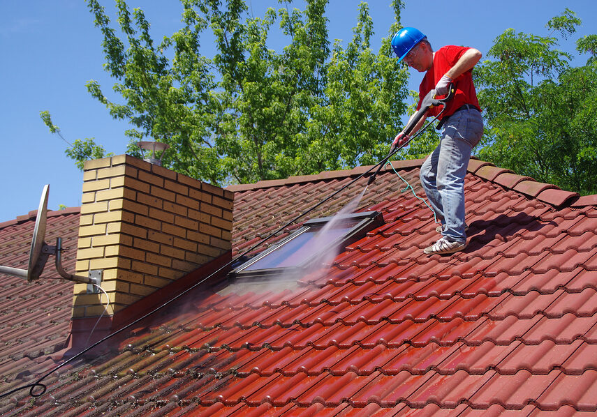 House Roof Cleaning With Pressure Tool. Worker On Top Of Buildin House roof cleaning with pressure tool. Worker on top of building washing tile with professional equipment. Moss removing with water.
